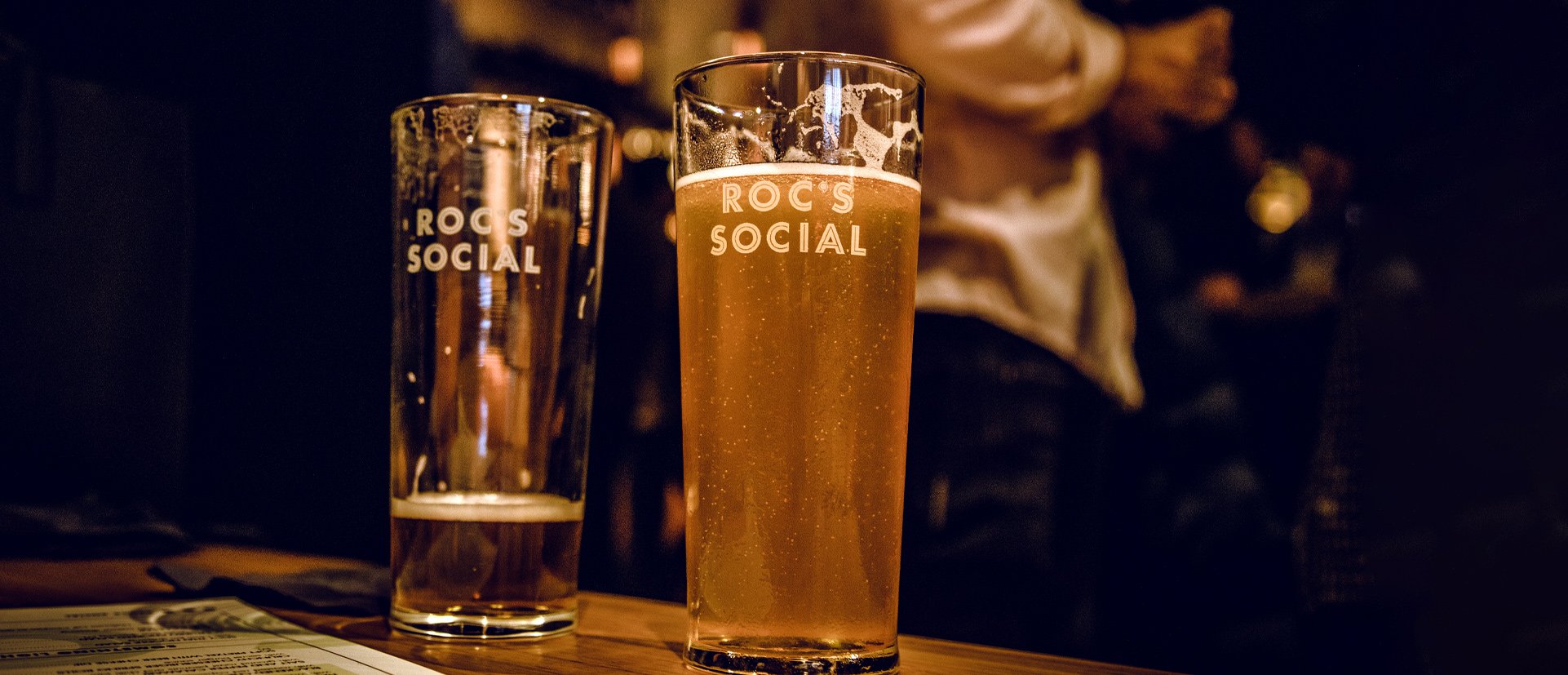 Two beer glasses display the Roc's Social logo